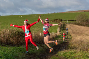 Two runners in festive attire enjoy the 3rd annual Lewes Downland Santa Run